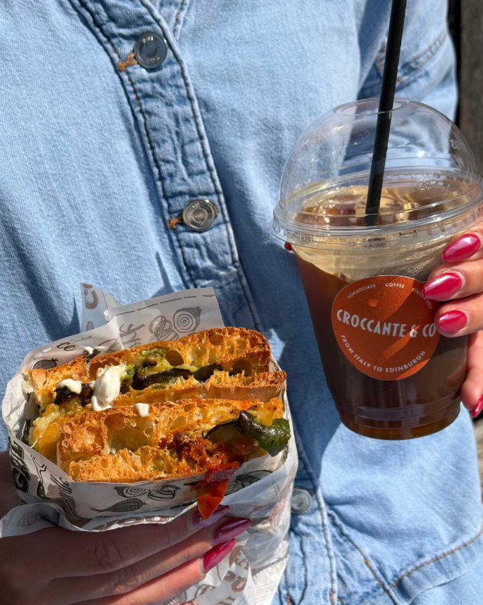 A filled schiacciata held beside an iced Croccante & Co coffee