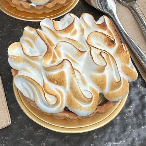 A lemon meringue tart on a gold board at Croccante & Co